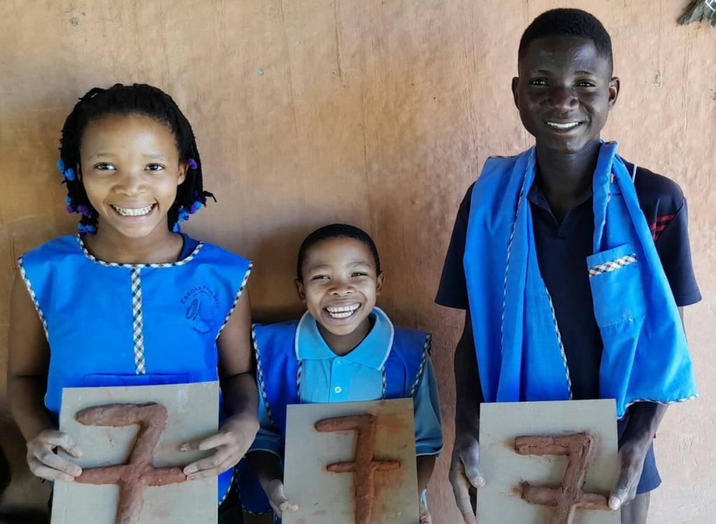 three smiling African children holding up the number seven written in sculpted mud