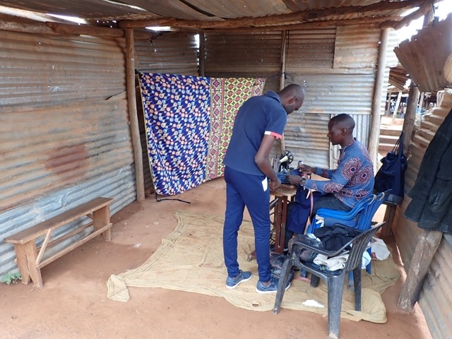 a man talks to a tailor at an open-air market african market