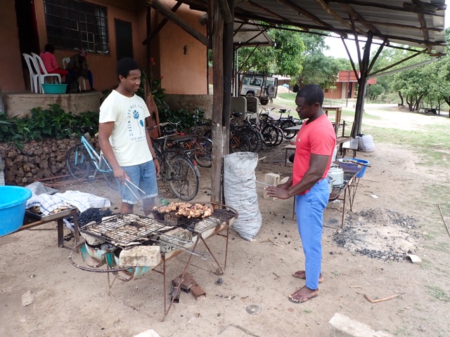 chicken and fish frying on a large grill attended by two men