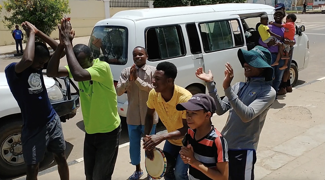 a group of people smile and dance on the sidewalk next to a truck and van