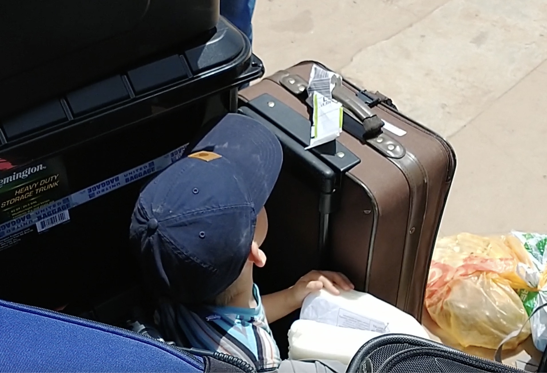 boy hiding in stack of baggage on sidewalk
