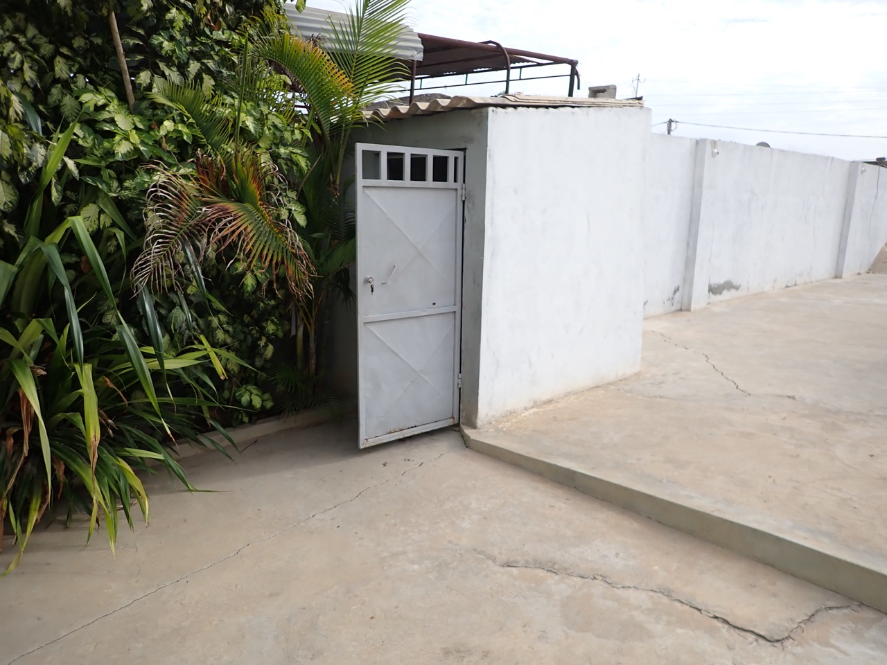 an outhouse in the concrete front yard of a walled compound