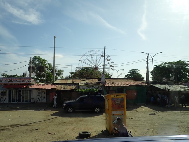 dirt street in front of rundown homes with a ruined ferris wheel in the background